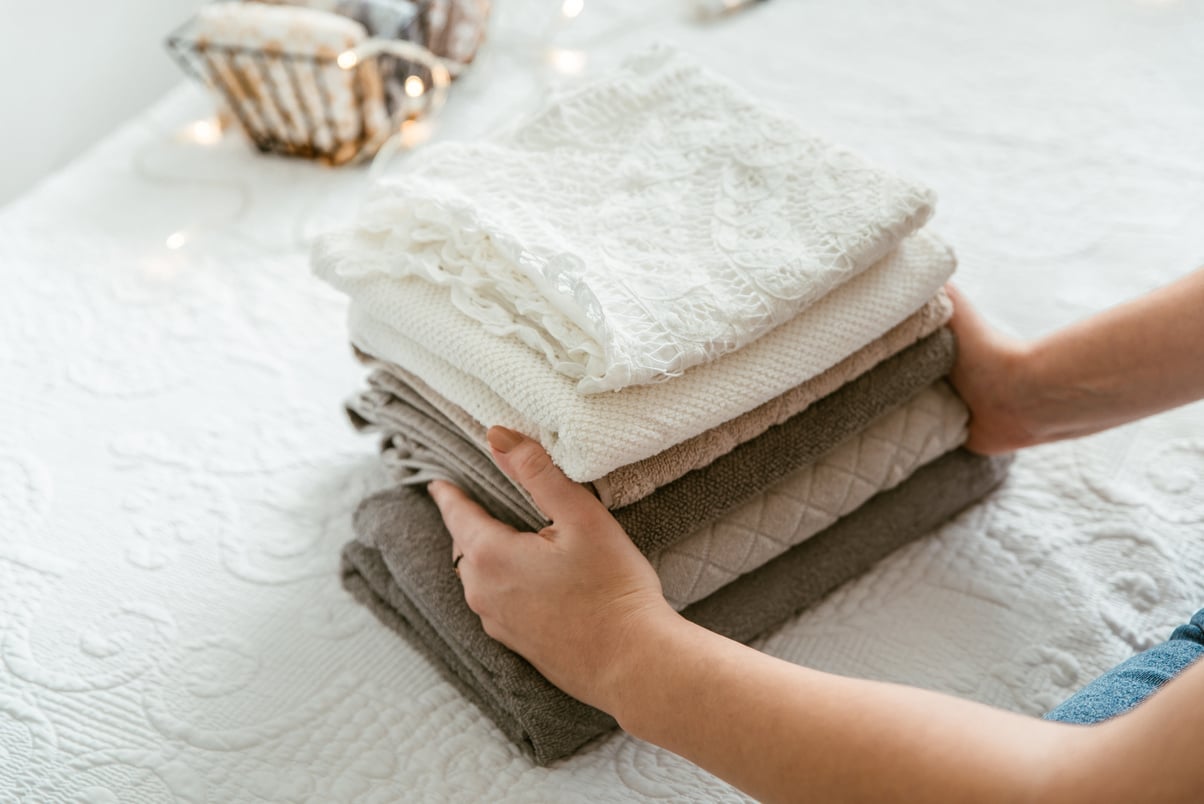 Woman folding stack of fresh laundry and towels, organizing laundry in boxes and baskets.